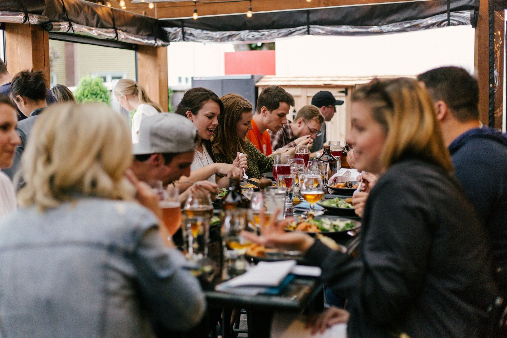 Guests laughing over drinks and food along a long communal table under string lights at a plant bingo night